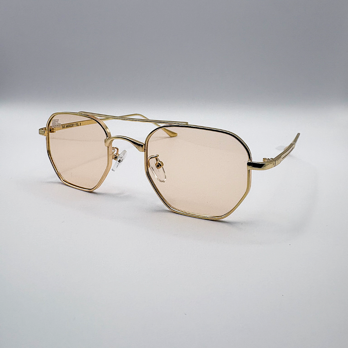 Gold-framed sunglasses with beige lenses on a light gray background